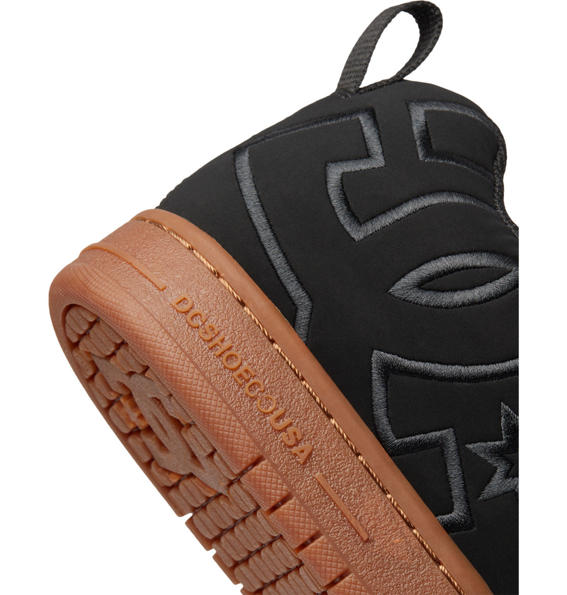 Close-up of the Men’s Court Graffik Shoes by DC Shoes in black with a brown sole, showcasing their signature puffy silhouette and intricate stitching. A prominent embroidered DC logo accents the side, while “DCSHOECOUSA” is embossed on the brown midsole above the distinctive grooved tread—hallmarks of this iconic DC Shoes design.