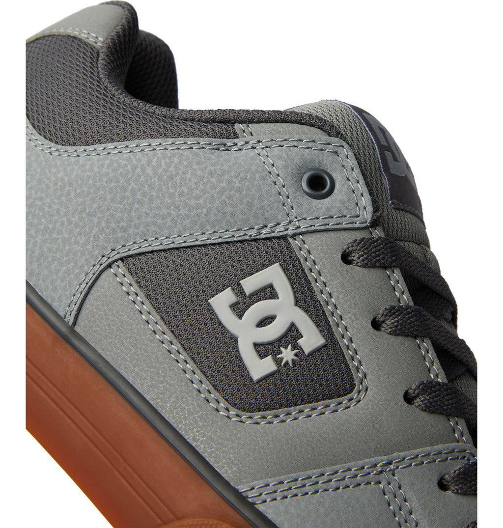 Close-up of a gray sneaker with black laces, textured detailing, and a brown sole. The DC Shoes Men’s Pure Shoes feature a bold white DC logo on the side panel, offering both comfort and versatile style for everyday wear.