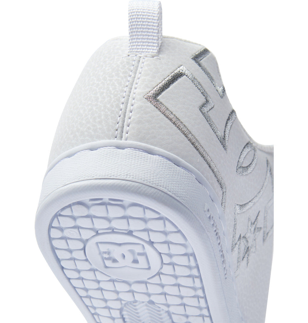 Close-up of the heel and sole of the Women’s Court Graffik Shoes by DC Shoes, featuring a white chunky silhouette with a textured surface. The patterned sole displays the DC Shoes logo, which also appears in metallic silver on the side of this ‘90s style women’s sneaker.