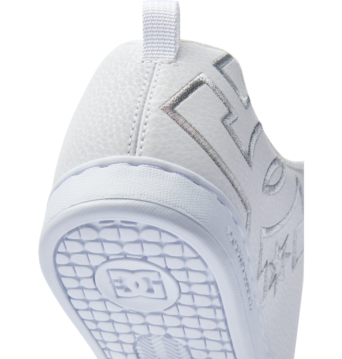 Close-up of the heel and sole of the Women’s Court Graffik Shoes by DC Shoes, featuring a white chunky silhouette with a textured surface. The patterned sole displays the DC Shoes logo, which also appears in metallic silver on the side of this ‘90s style women’s sneaker.