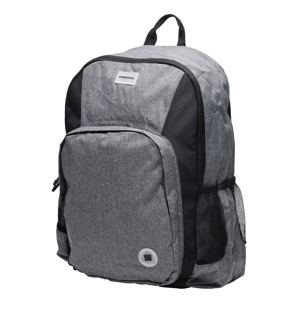 The DC Shoes Locker Backpack is gray and black, featuring a spacious front pocket, mesh side pockets, a top handle, a small round grommet on the front, and a padded laptop sleeve for added protection.