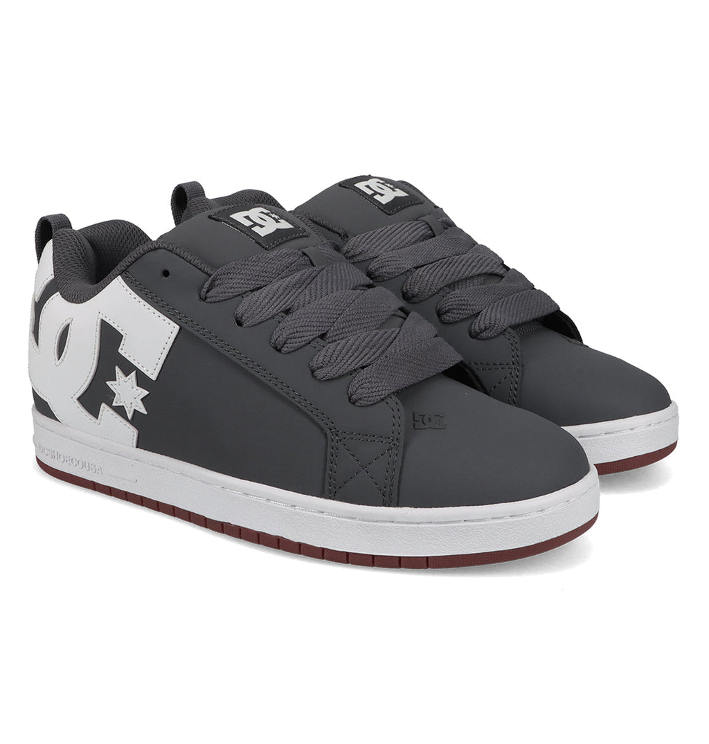 A pair of Men’s Court Graffik Shoes by DC Shoes, featuring a chunky gray design with thick gray laces, white soles, and a prominent white DC logo on the side, displayed on a white background.