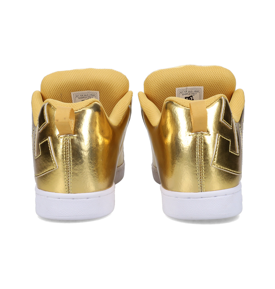 A pair of DC Shoes Women’s Court Graffik Shoes in gold metallic, featuring white soles, yellow inner linings, and a geometric pattern on the heel—displayed from the back and channeling a chunky ’90s style.