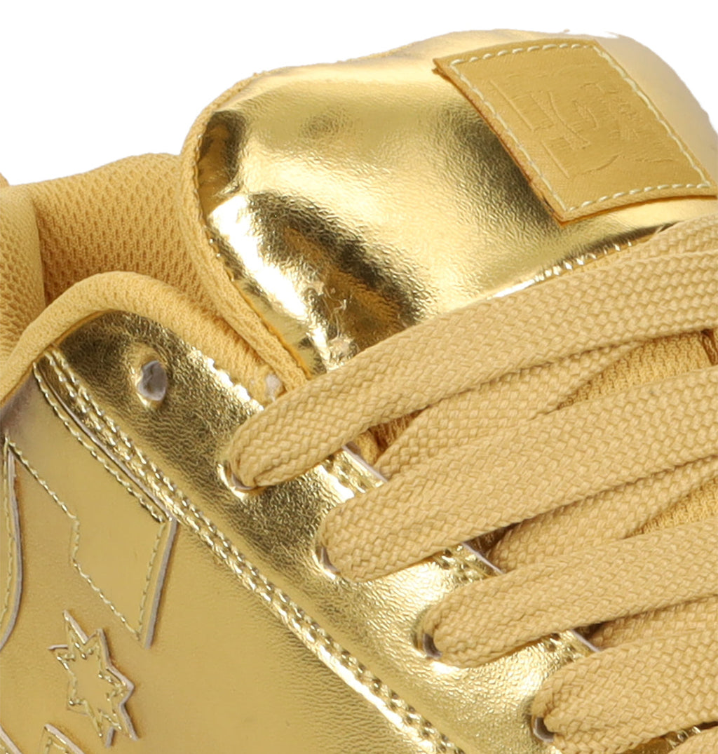 Close-up of the DC Shoes Women’s Court Graffik Shoes in shiny gold with gold laces and textured fabric. Embossed stars and DC branding details appear on the side and tongue, capturing the bold, chunky ‘90s style of women’s sneakers.