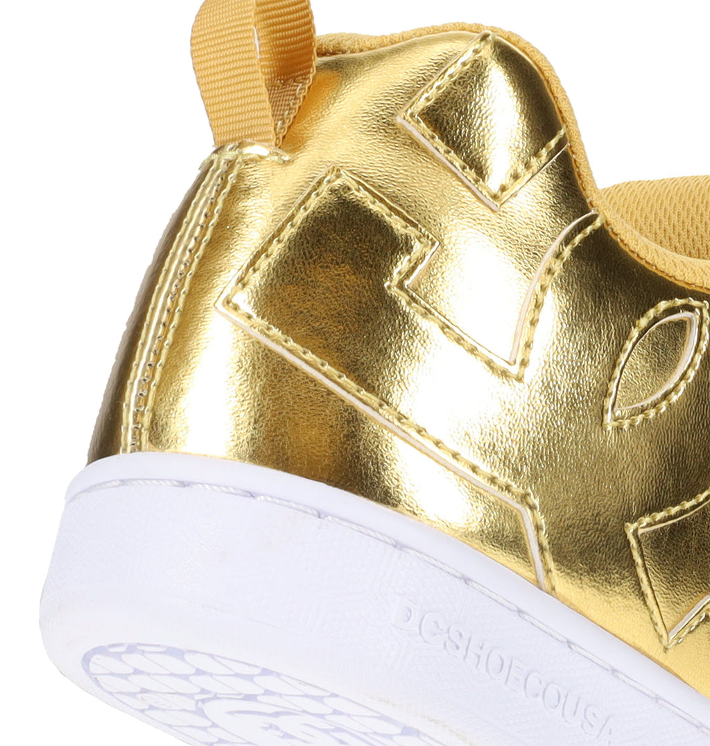 A close-up of the heel of the DC Shoes Women’s Court Graffik shows a gold metallic sneaker with a textured white sole and yellow fabric accents. This chunky ‘90s style shoe features embossed patterns and detailed stitching, offering a bold and stylish look.