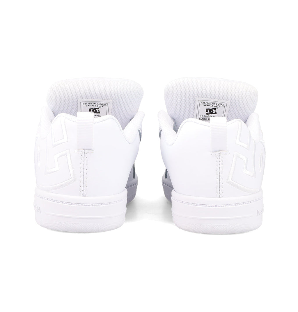 The Kids' Court Graffik Shoes by DC Shoes are white sneakers shown from the back, featuring embossed heel patterns, visible inner tongue labels, white soles, and stitching accents for a classic skate-inspired look.