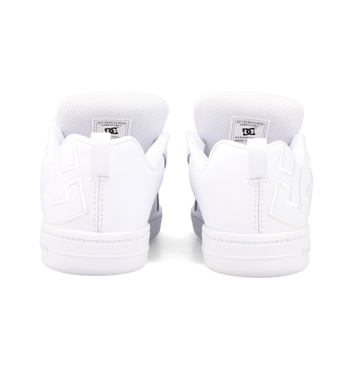 The Kids' Court Graffik Shoes by DC Shoes are white sneakers shown from the back, featuring embossed heel patterns, visible inner tongue labels, white soles, and stitching accents for a classic skate-inspired look.