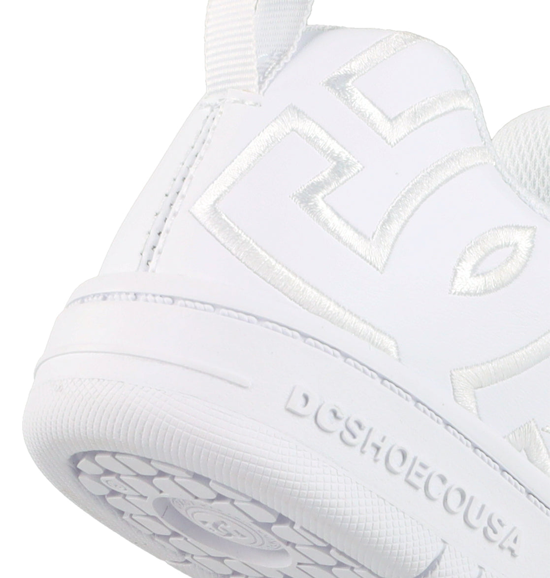 Close-up of the heel and side of DC Shoes Kids' Court Graffik Shoes, featuring raised white stitching in a stylized logo. The textured sole displays embossed DCSHOECOUSA text, highlighting their skate-inspired design for kids.