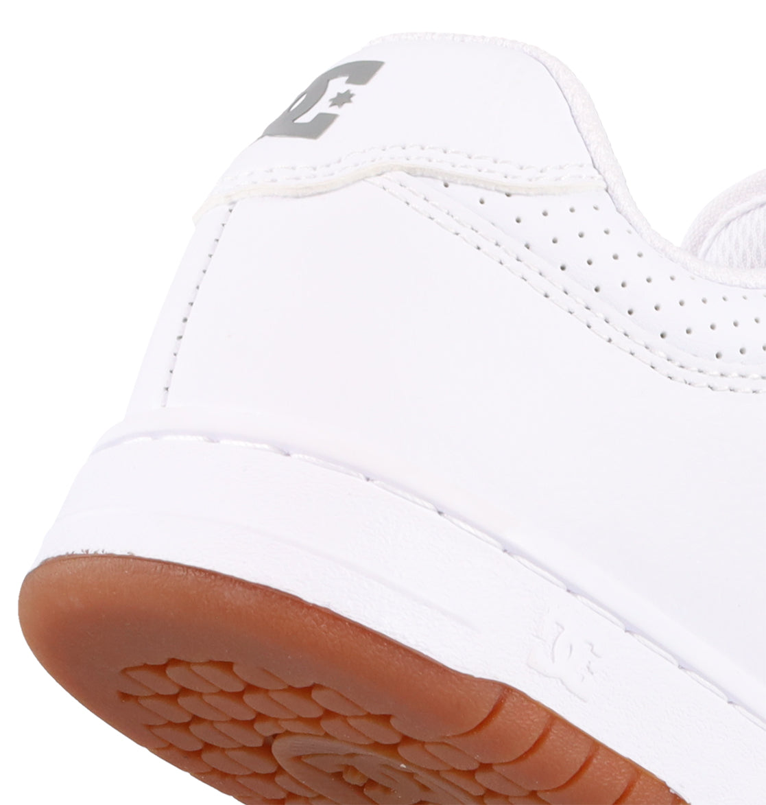 Close-up of the heel of a white Women's Manteca 4 Shoe by DC Shoes, featuring a brown rubber sole, gray DC Shoes logo on the back, and perforated detailing near the collar for a performance-focused look.