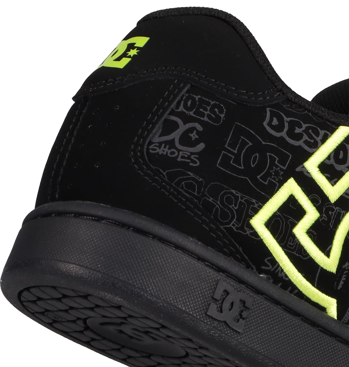 Close-up of the heel of a black DC Shoes Men's Net Shoe with neon yellow accents and a grey logo. This sneaker features strong DC branding, durable fabrics, and a textured black sole with a small DC Shoes logo on the side.
