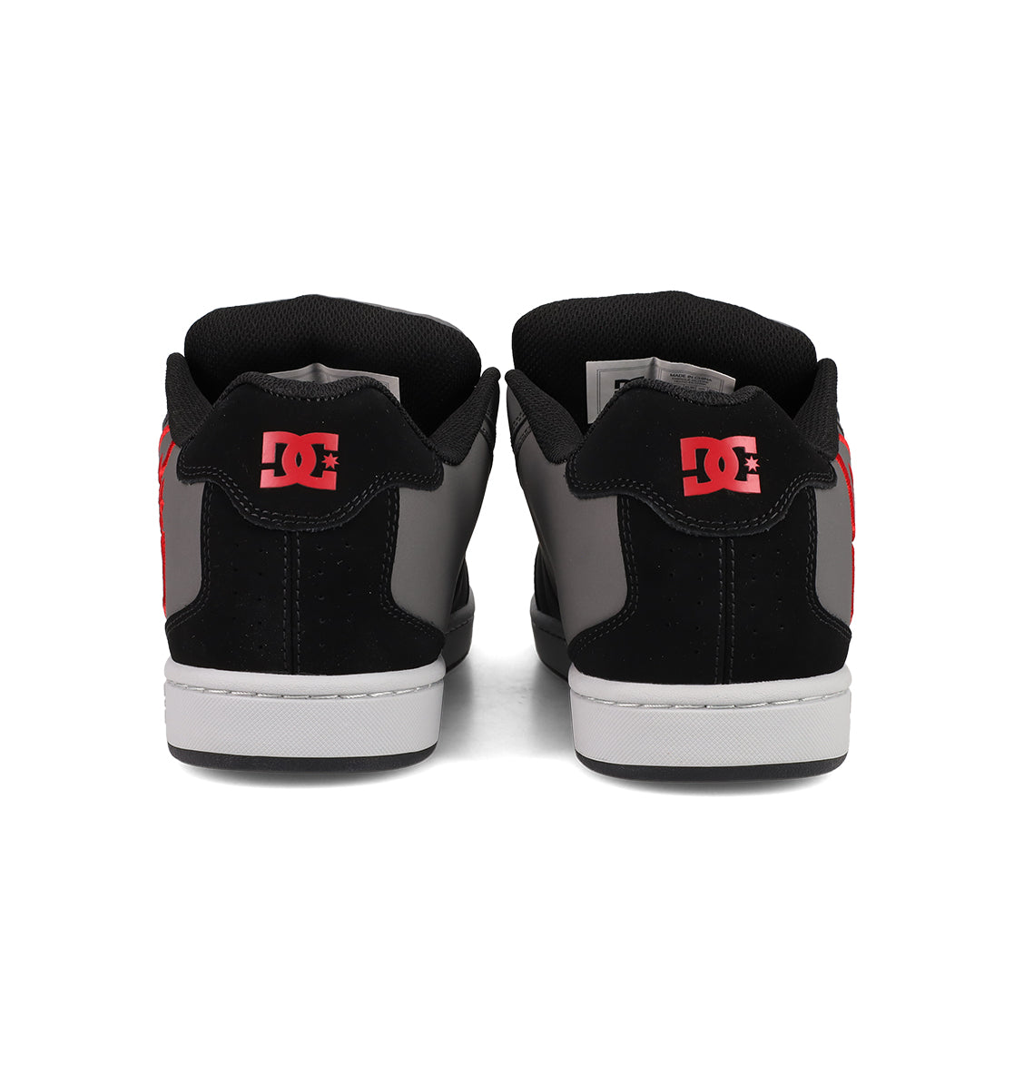 A pair of DC Shoes Men's Net Shoes shown from the back feature black, gray, and red colors with bold red DC branding on the heel. These puffy sneakers have white soles, black collars, and are made from durable fabrics.