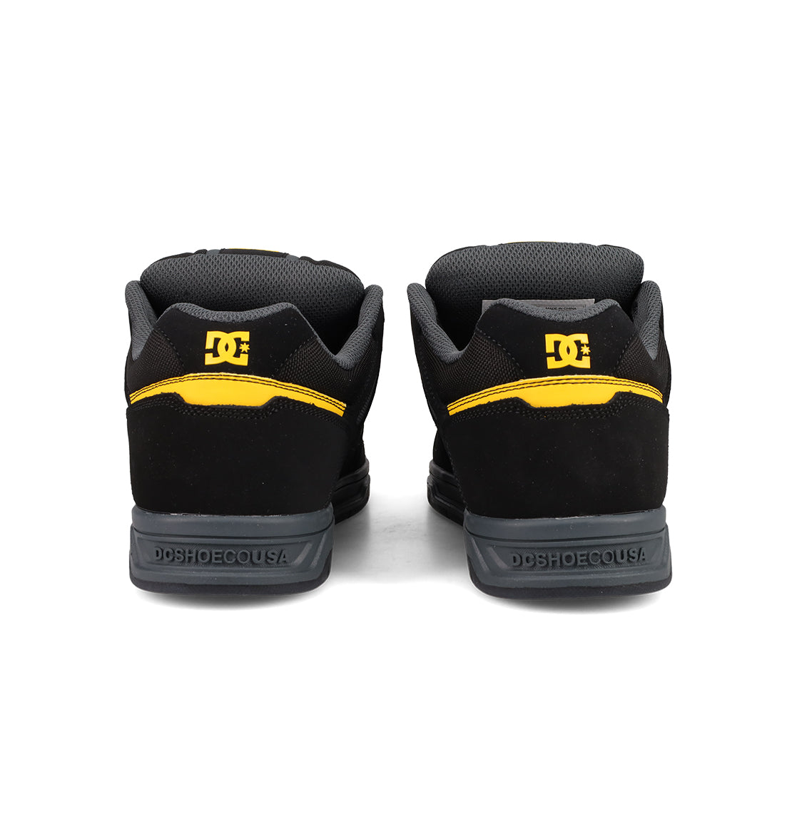 The Men's Stag Shoes by DC Shoes in black with yellow accents and logo detail on the heels feature a durable cupsole, shown from the back on a white background—ideal for authentic skate culture.