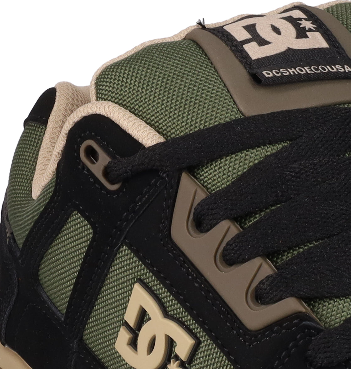 Close-up of Men's Stag Shoes by DC Shoes in green and beige, showcasing textured fabric, black laces, cupsole construction, and DC logos on the side and tongue.