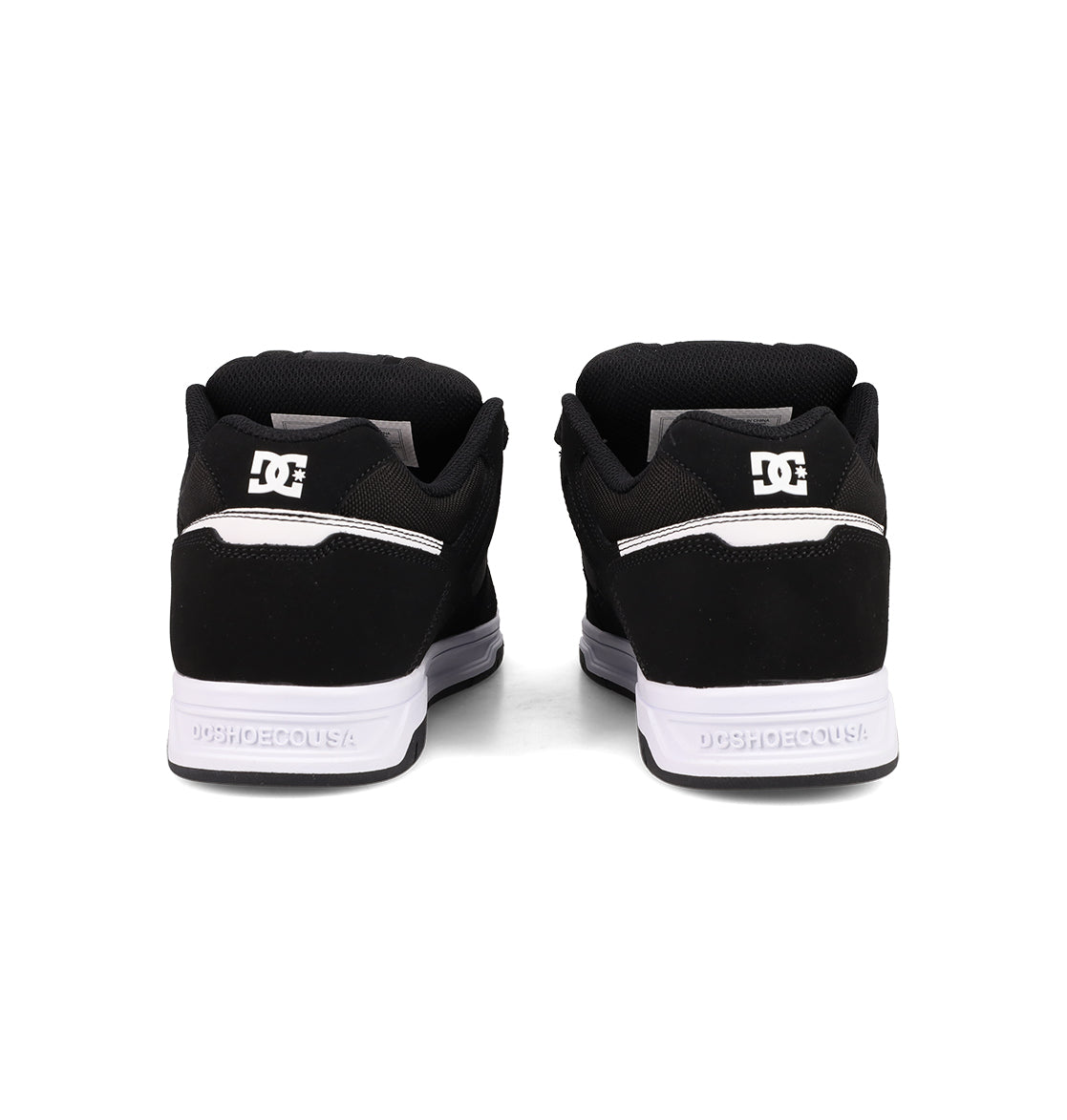 Rear view of a pair of Men's Stag Shoes by DC Shoes, featuring black uppers, white cupsoles, and the DC logo in white on the heel, positioned side by side against a white background.