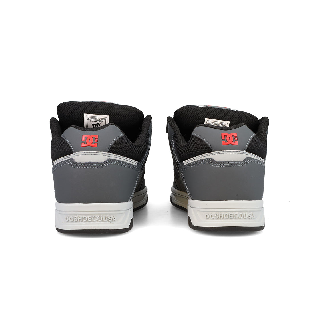 A pair of Men’s Stag Shoes by DC Shoes in gray and black are seen from the back, featuring a red DC logo on each heel and “DCSHOECOUSA” text on the midsoles—a classic nod to skate culture.