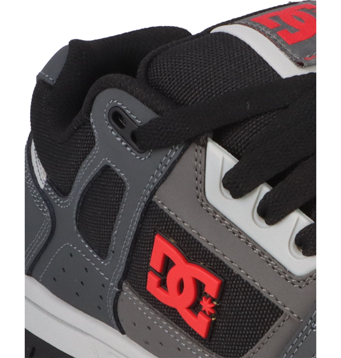 Close-up of the DC Shoes Men’s Stag sneaker in black and grey, featuring a red DC Shoes logo, white and black laces, mesh fabric accents, and a durable cupsole inspired by skate culture.