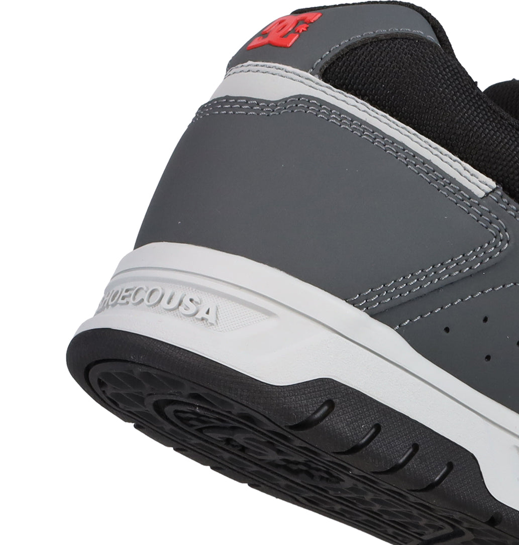 Close-up of the heel of a gray and white DC Shoes Men’s Stag Shoe with black and red accents, showcasing the red DC logo and “SHOECOUSA” embossed on the white midsole. Built with durable cupsole construction, this sneaker pays tribute to skate culture.