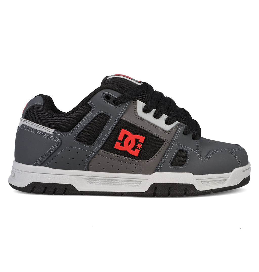 The Men’s Stag Shoes from DC Shoes are gray and black skate shoes featuring a red DC logo on the side, black laces, and a white and black sole. Designed with cupsole construction for enhanced durability, these low-profile sneakers offer padded support, perfectly embodying classic skate culture style.