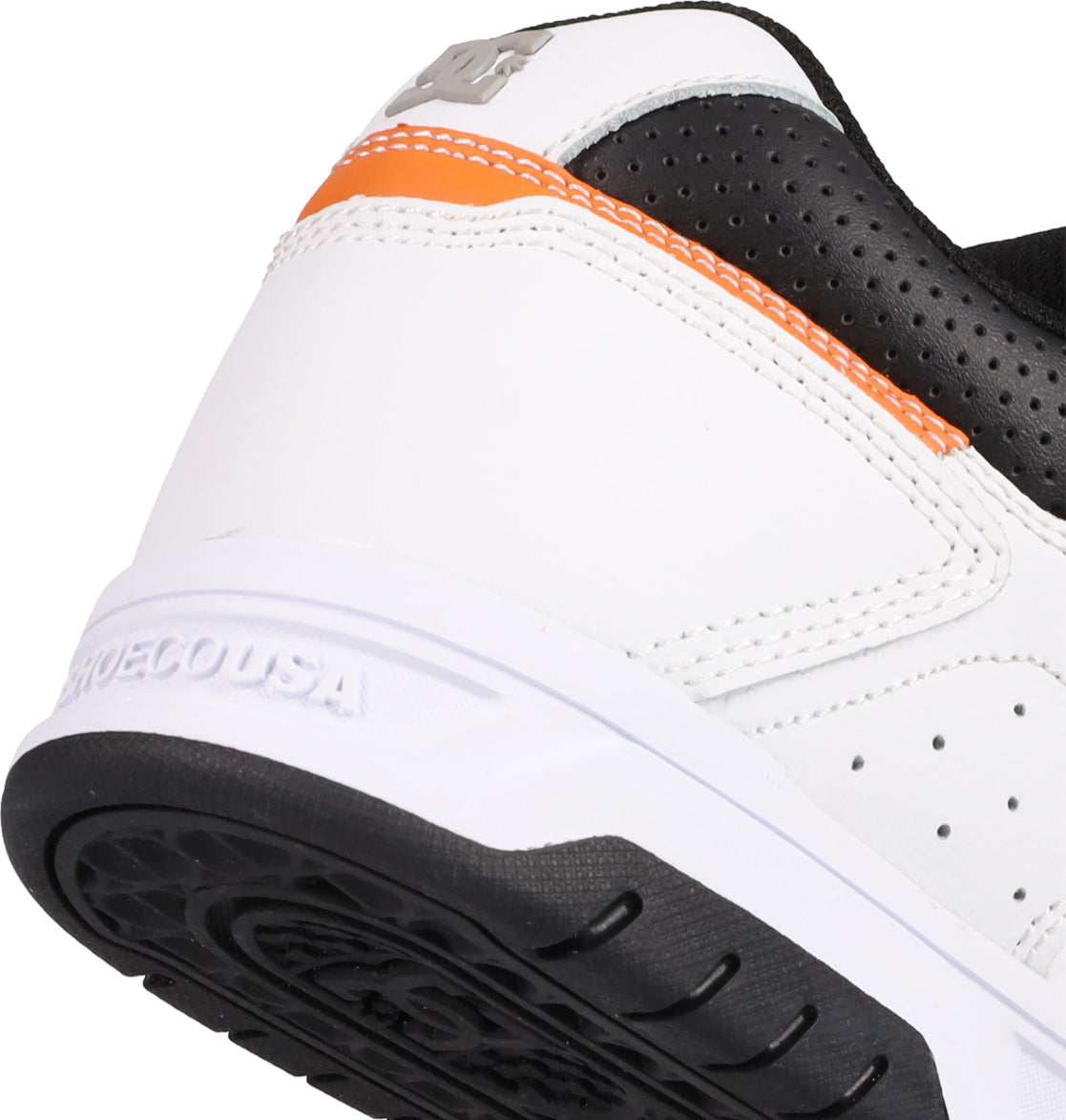 Close-up of the heel of a white Men's Stag Shoe by DC Shoes, featuring black and orange details, a textured cupsole, visible stitching, an embossed brand logo on the heel, and SHOECOUSA molded into the rubber sole—a nod to skate culture.