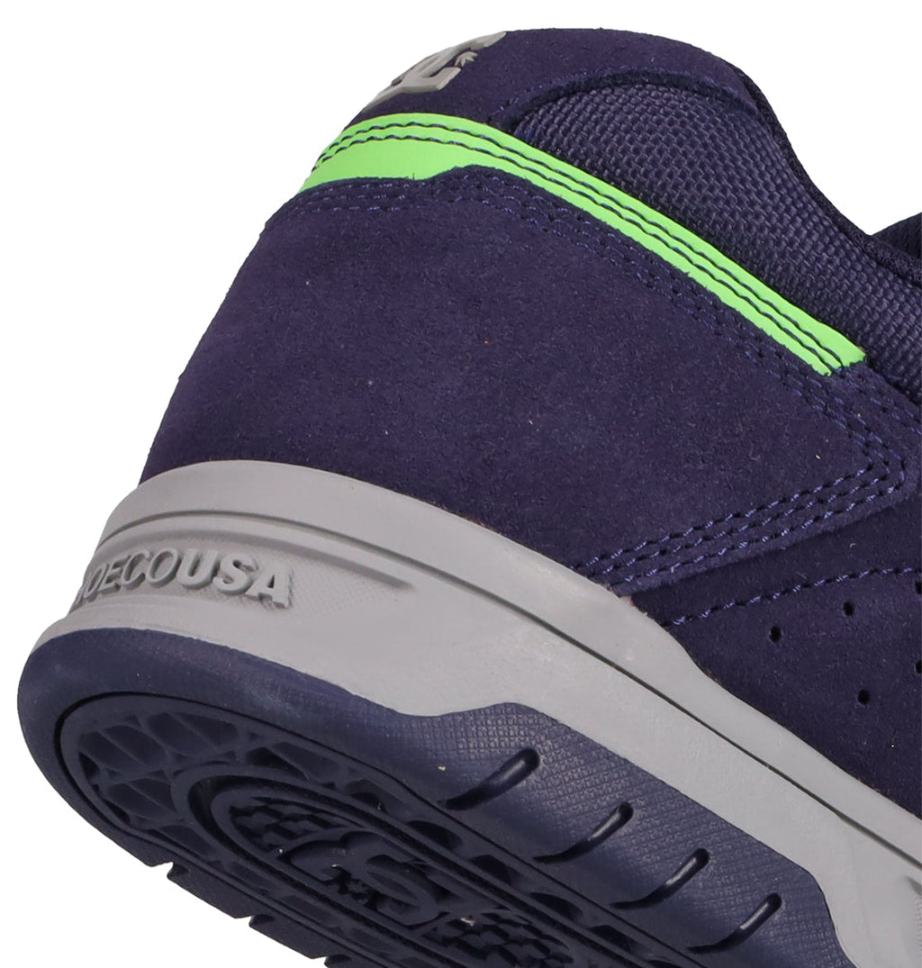 Close-up of the heel of DC Shoes Men's Stag Shoes, a navy blue suede sneaker with gray cupsole, neon green back detail, visible stitching, and DECOUSA embossed on the heel—showcasing skate culture style.