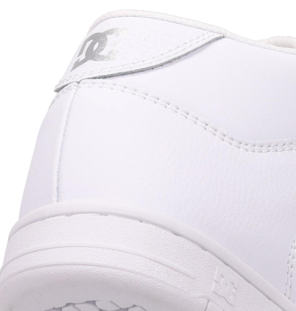 Close-up of the heel of a white Women’s Manteca 4 Hi High-Top Shoe from DC Shoes, featuring textured leather and a silver DC Shoes logo on the back. The performance-driven design showcases detailed stitching and a robust sole, highlighting both style and lasting durability.