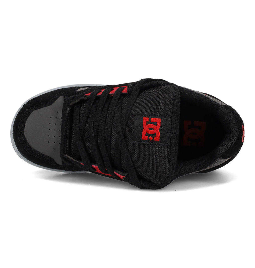 The Kids’ Stag Shoes by DC Shoes are shown from above in black and gray, featuring a red DC Shoes logo on the tongue. This sneaker includes black laces, red eyelets, and durable rubber outsoles engineered for lightweight cushioning and enhanced impact absorption.