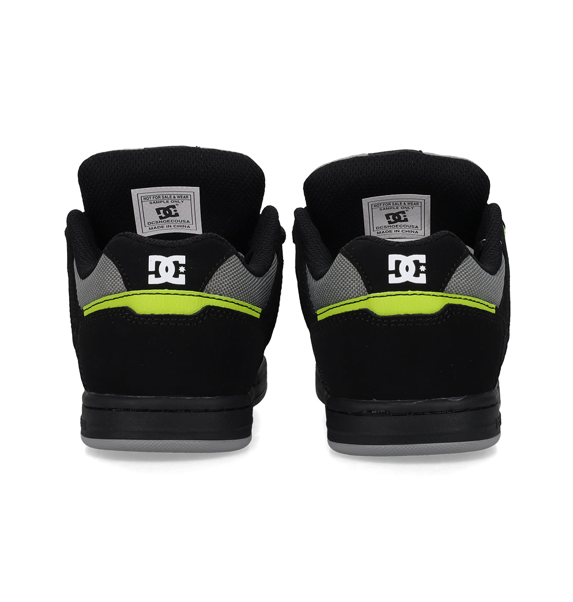 Back view of a pair of Kids’ Stag Shoes by DC Shoes in black with gray accents and a neon yellow stripe, showcasing the iconic DC logo on the heels and inner labels. This minimal silhouette offers everyday versatility as a go-to vulc shoe for effortless style and comfort.