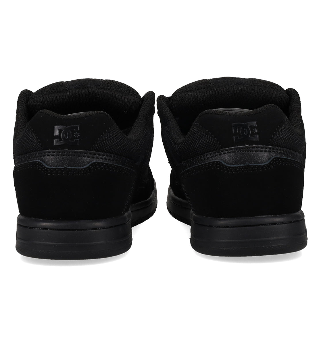 A pair of Kids’ Stag Shoes by DC Shoes in black, viewed from behind to highlight the heel, durable cupsole, and the logo on the back of each shoe against a white background.