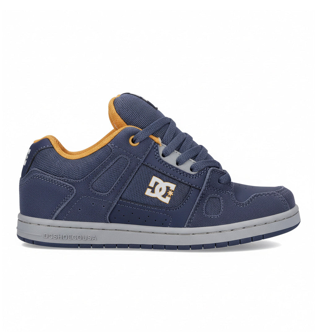 A side view of the Kids’ Stag Shoes by DC Shoes in navy blue with mustard yellow accents, grey sole, and laces is shown on a white background, highlighting a minimal silhouette that makes them an everyday go-to.