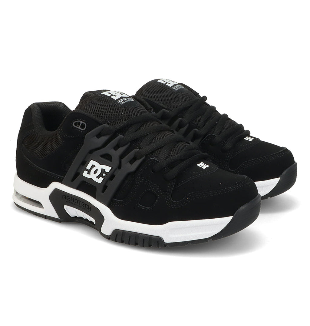 A pair of Men’s AT-2 Shoes by DC Shoes in black, featuring white midsoles, black laces, and the DC logo in white on the side and tongue. These sneakers showcase a chunky silhouette with visible AEROTECH branding on the side, providing cushioned impact and enhanced breathable comfort through advanced AEROTECH ventilation technology.