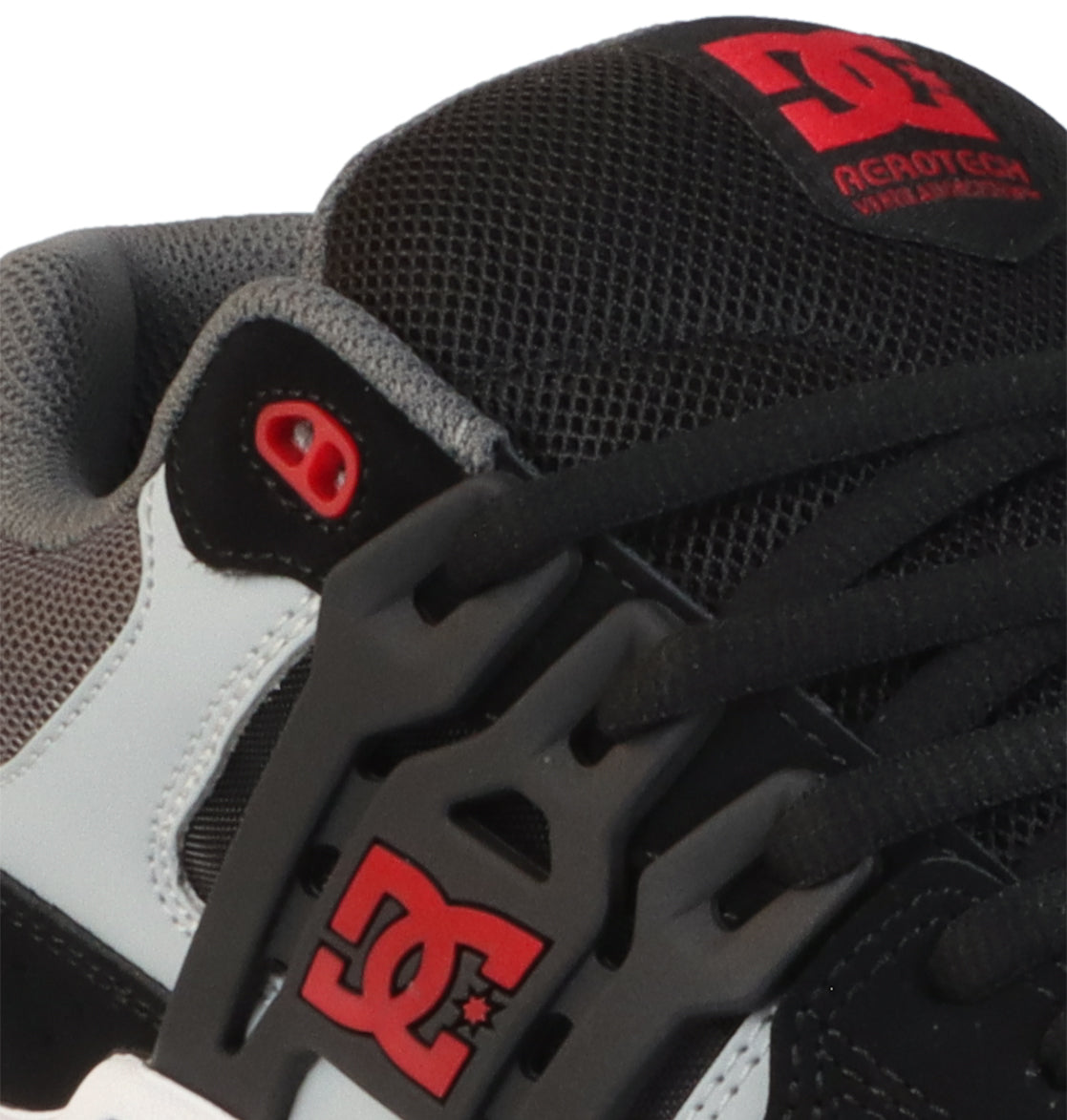 Close-up of the DC Shoes Men’s AT-2, a skate shoe in black, gray, and white with red DC branding on the tongue and side. Features include thick black laces, gray mesh padding on the upper for comfort, and a supportive TPU cage that adds stability and structure to the design.
