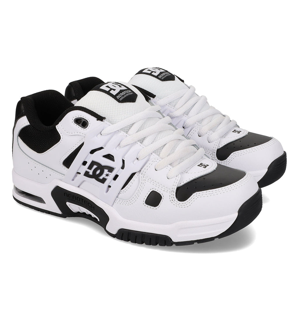 A pair of Men’s AT-2 Shoes by DC Shoes featuring black and white mesh and leather accents, lace-up design, a supportive TPU cage for enhanced stability, and a thick sole.