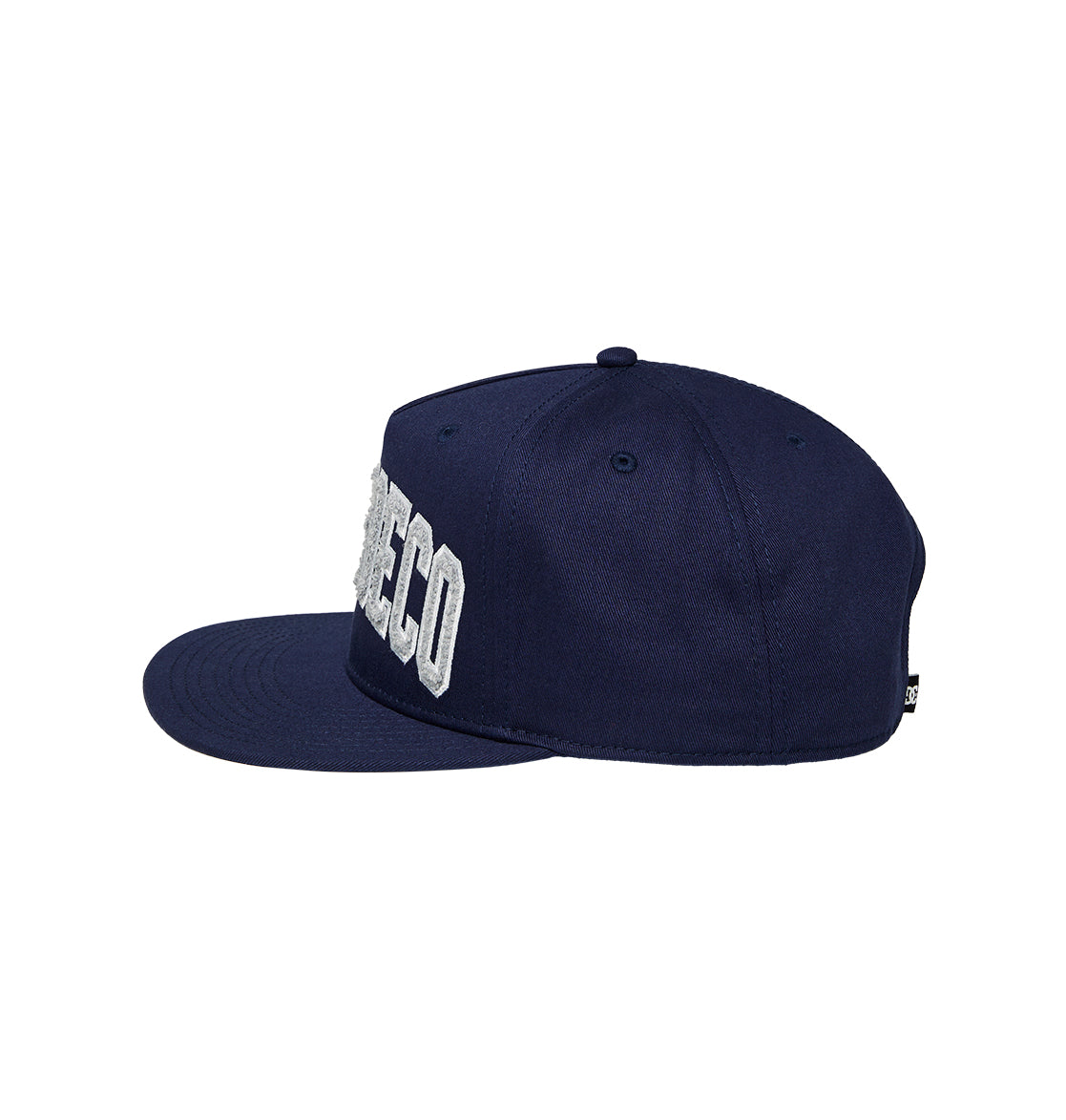 A navy blue flat-brim University Cap Snapback by DC Shoes, featuring large white embroidered letters partially visible on the front, is displayed from the side against a white background—ideal for bringing a streetwear-inspired edge to any outfit.