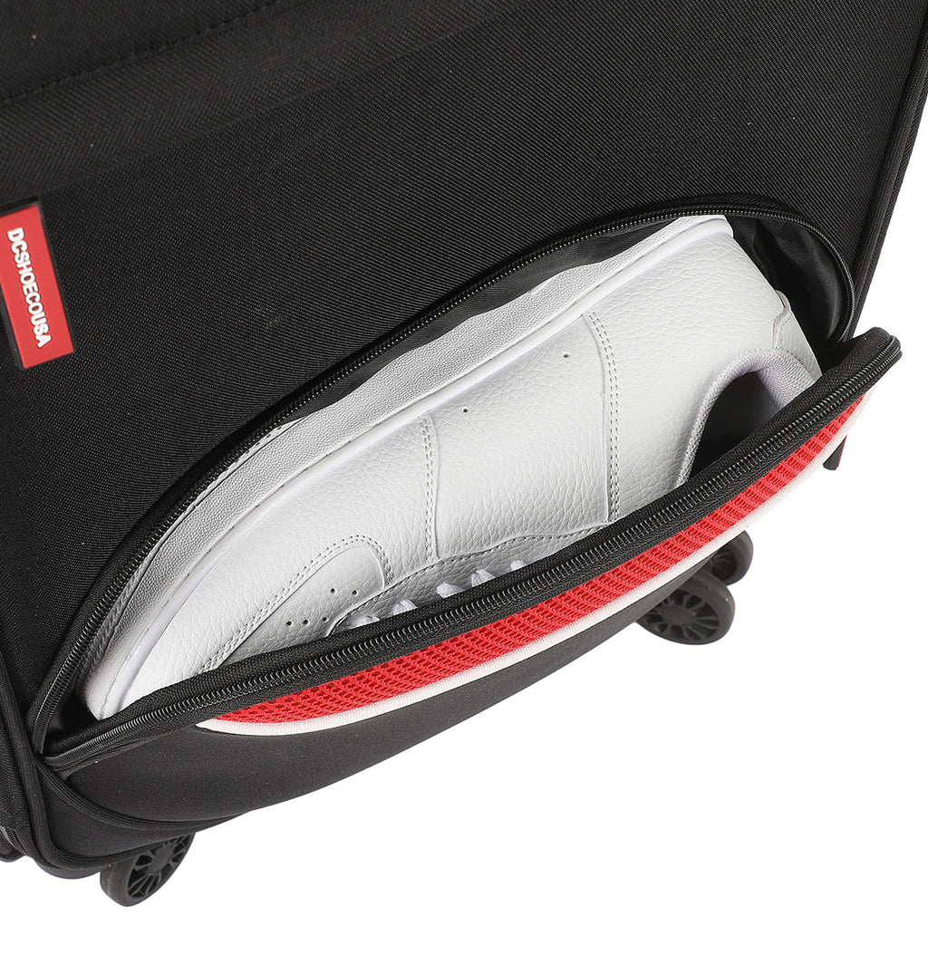 A close-up of the DC Shoes DC Runner Carry-On's black pocket, partially unzipped to reveal a white sneaker inside, with a red accent along the zipper.
