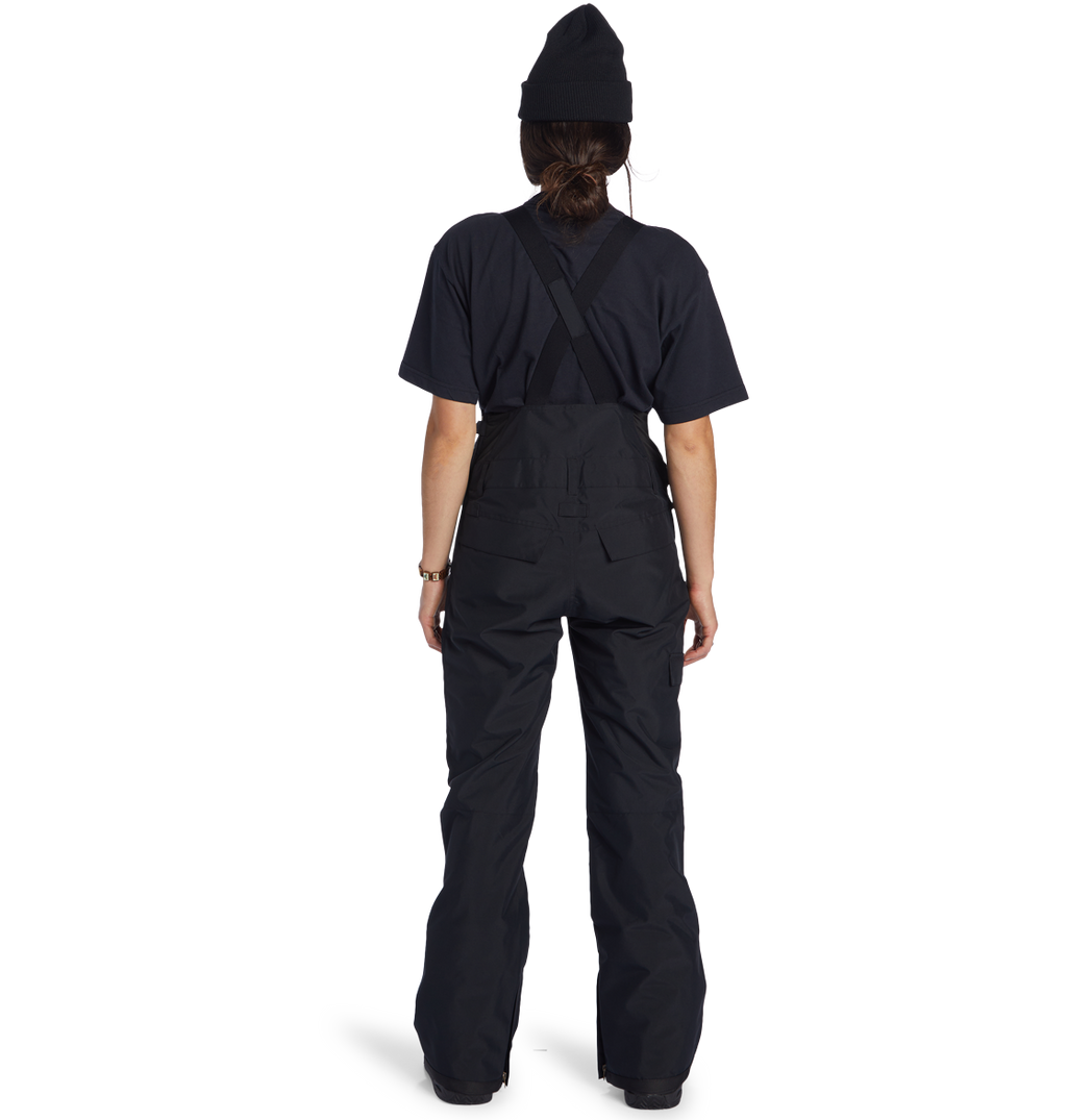 A person wearing the DC Shoes Women’s Valiant Bib, a black t-shirt, and a black beanie stands facing away against a plain white background.