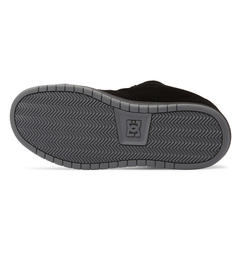 The image displays the gray rubber sole of the Men’s Gaveler Shoes by DC Shoes, featuring a herringbone tread pattern and a raised logo at the center. The chunky design enhances its durable leather construction, offering a blend of style and sturdiness.