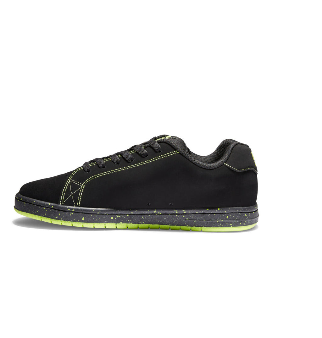 A side-view image of the Men’s Gaveler Shoes by DC Shoes shows a black chunky sneaker crafted from durable leather, featuring green speckled soles, green stitching, and black laces, displayed against a white background.
