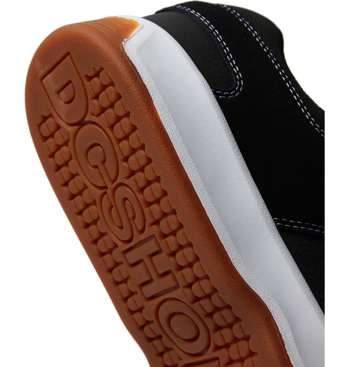 Close-up of the sole of a black Men’s Lynx Zero Shoe by DC Shoes, featuring white stitching and a brown rubber bottom embossed with “DCSHOE,” highlighting the iconic skate shoe style of this classic model.