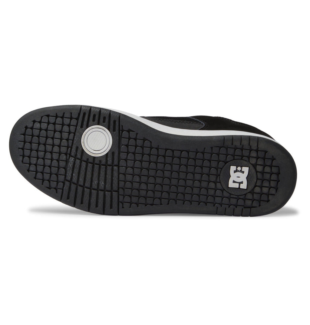The image displays the black rubber sole of the Men’s Manteca 4 Shoes by DC Shoes, which features a circular tread pattern near the toe and a signature square logo with a crown and stylized E at the heel, emphasizing its performance-oriented design.