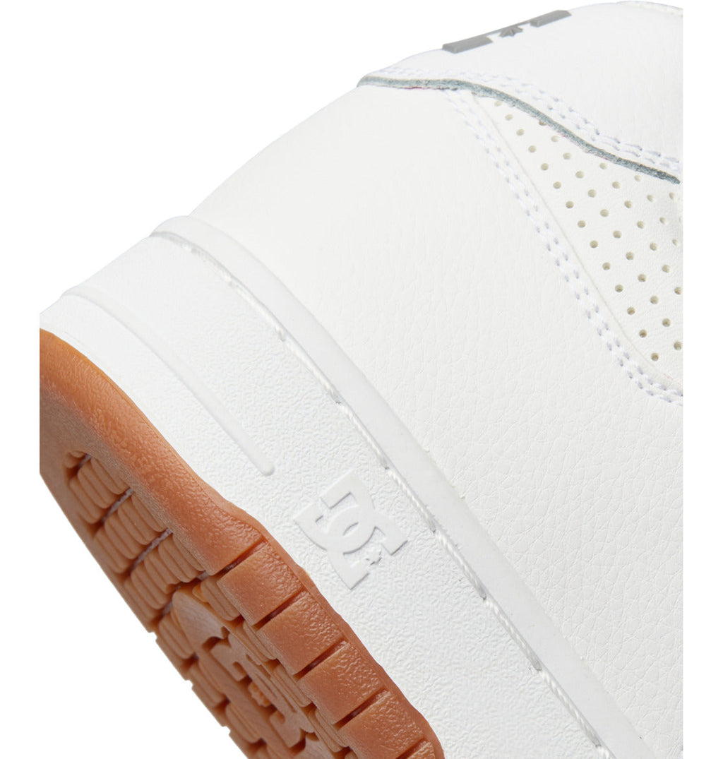 Close-up of a white Men’s Manteca 4 Shoe by DC Shoes, featuring a textured light brown sole. The iconic DC Shoes logo is embossed near the heel, emphasizing the signature Manteca design. Its leather upper showcases perforated detailing for added style and durability, blending classic appeal with performance sneaker quality.