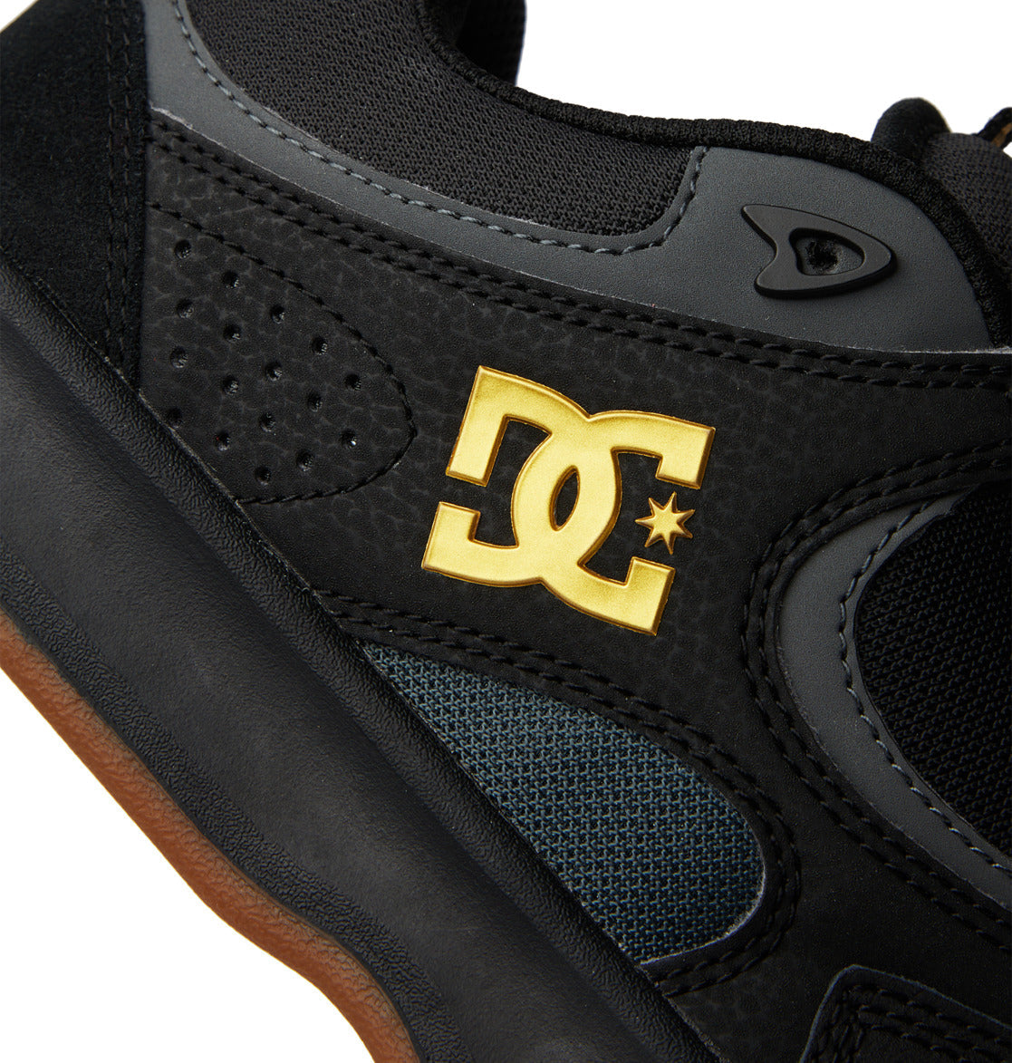 Close-up of the Men’s Kalynx Zero Shoes by DC Shoes in black, showcasing the gold DC Shoes logo on the side, textured and perforated details inspired by the classic Kalynx Zero design, and part of the brown rubber sole.