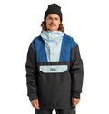 A man with long hair and a mustache wears a black beanie and the DC Shoes Men’s DC-43 Anorak Jacket in a color-blocked design of blue, black, and light blue with a front pocket, standing facing the camera.