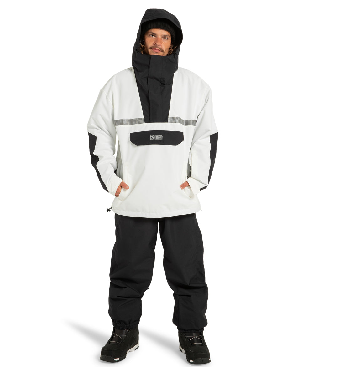 A man stands facing forward against a plain white background, wearing the DC Shoes Mens’ DC-43 Anorak Jacket in black and white—crafted from recycled polyester—paired with matching black pants and black boots.
