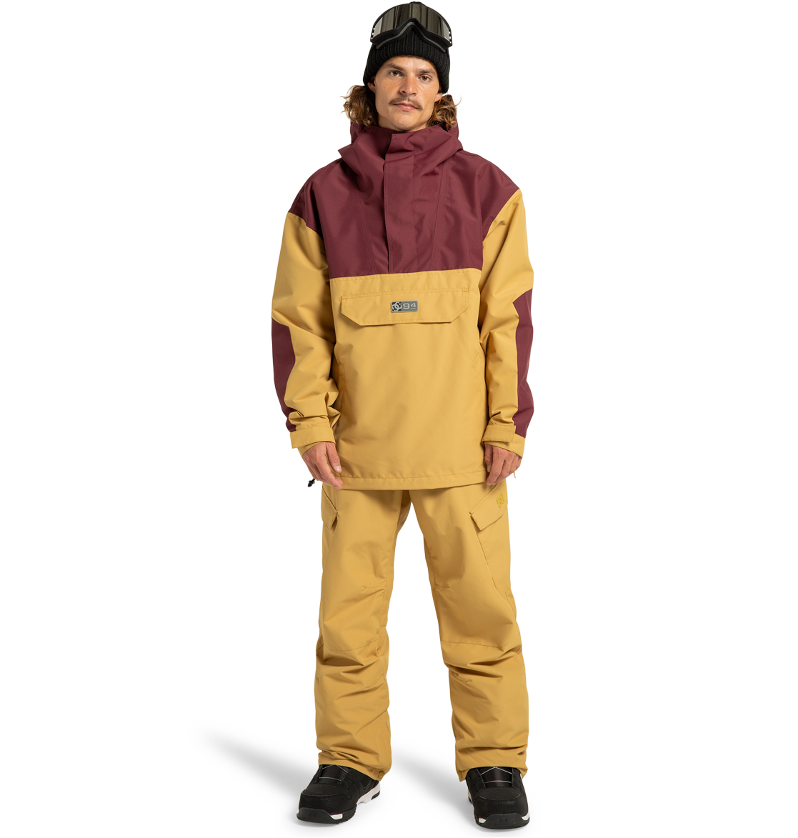 A person wearing the men’s DC-43 Anorak Shell Jacket by DC Shoes in yellow and maroon, paired with matching yellow snow pants, black gloves, black boots, a black beanie, and ski goggles stands against a plain white background.