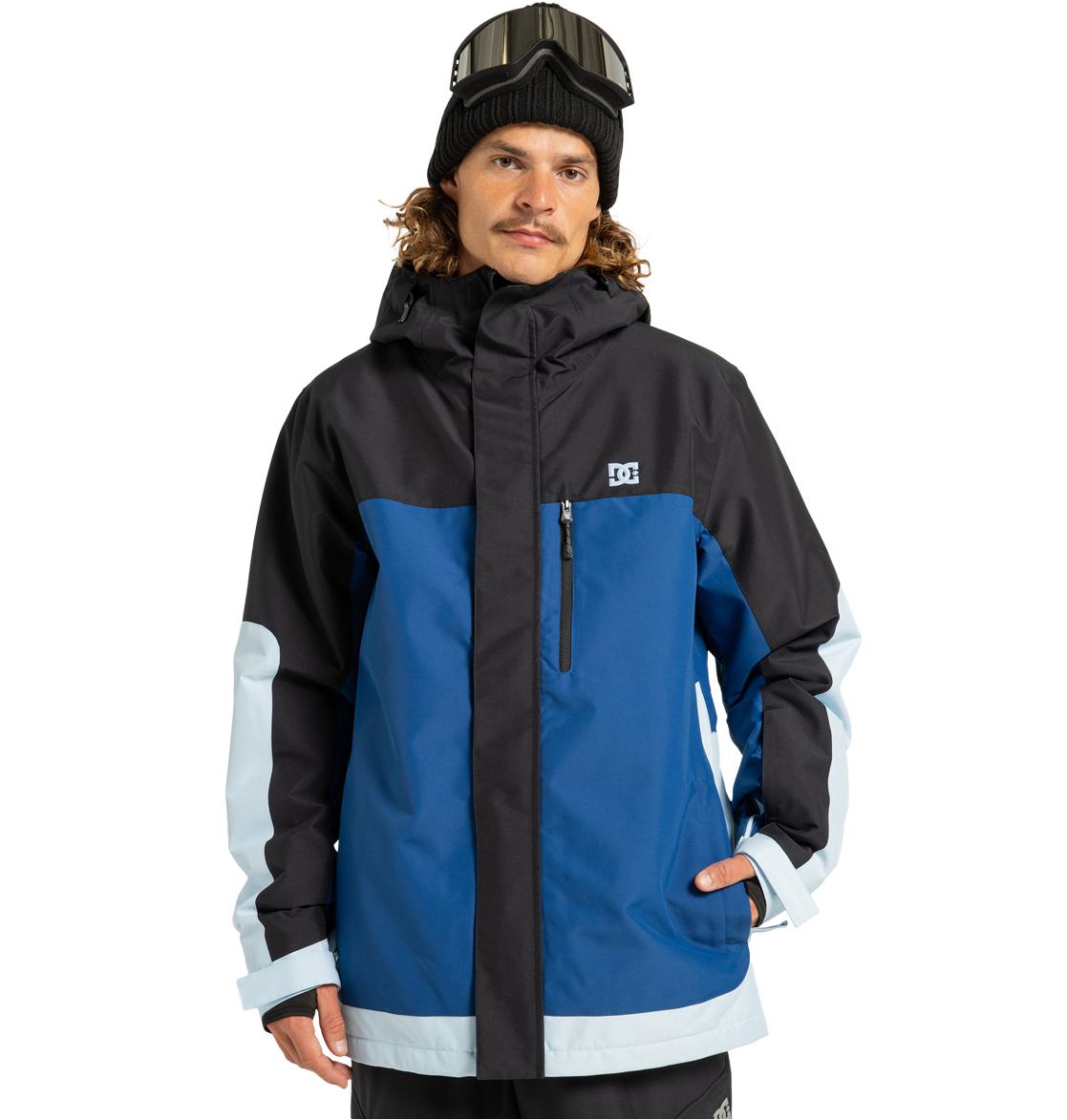 A man wearing the DC Shoes Men’s Defiant Insulated Jacket—crafted from recycled polyester in blue, black, and light blue with Weather Defense 10 technology—stands against a white background with one hand in his pocket, accessorized with a black beanie and ski goggles.
