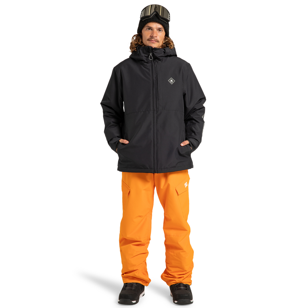 A person wearing the DC Shoes Unisex Basis Insulated Jacket, orange snow pants, black boots, a black beanie, and ski goggles stands facing forward against a plain white background.
