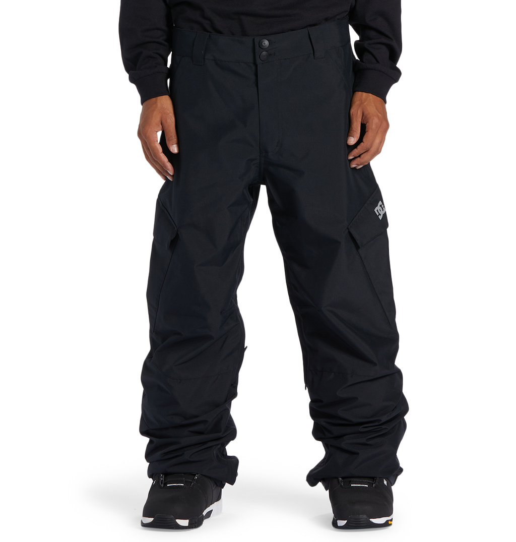 A person wearing loose-fitting black DC Shoes Men’s Banshee Insulated Pants, paired with a black sweatshirt and black sneakers, stands against a plain white background. The pants, designed as essential winter gear by DC Shoes, feature side pockets and a small white logo on the left thigh.