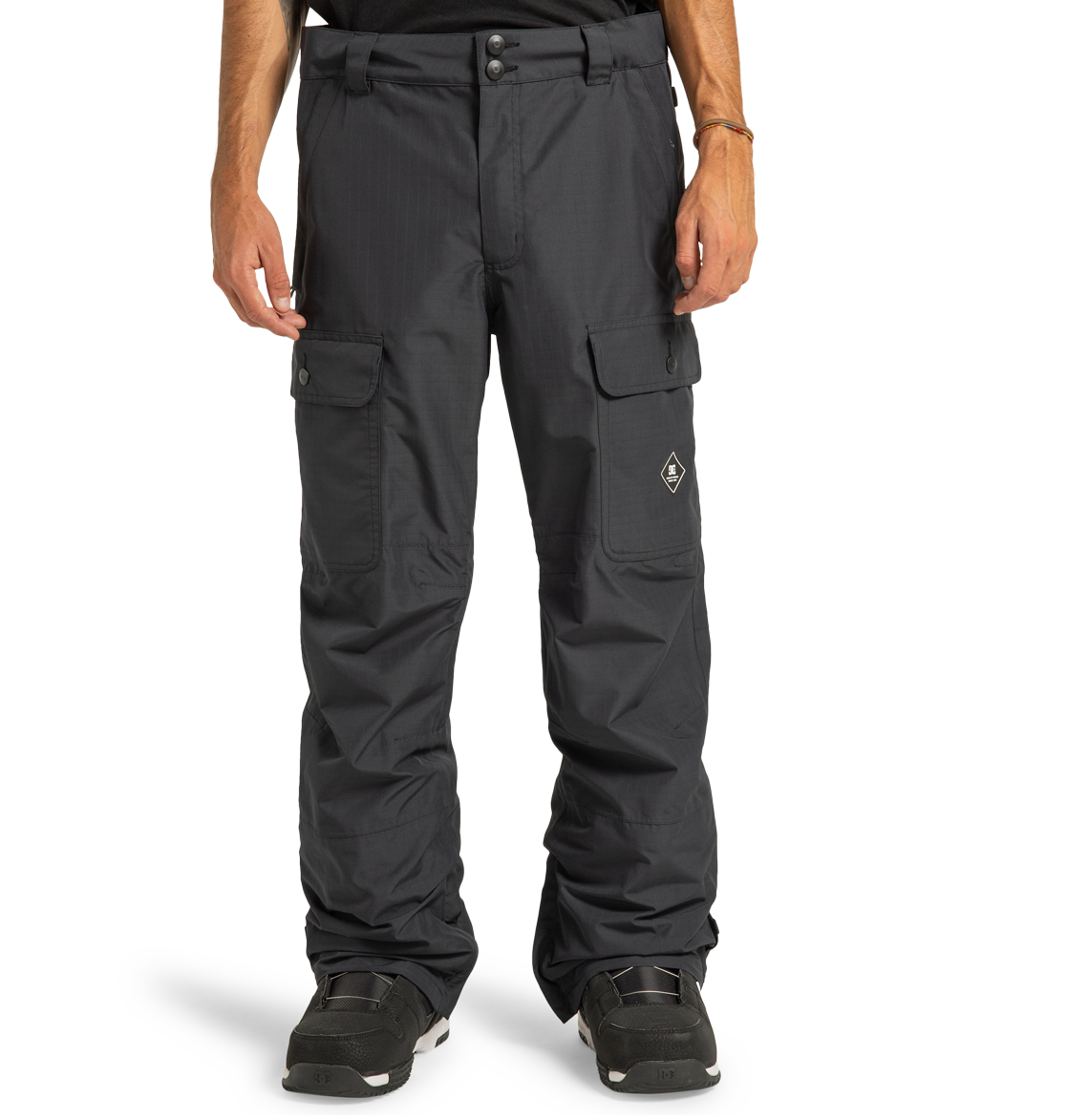 A person wearing DC Shoes Men’s Code Shell Pants, paired with black shoes and a bracelet, stands against a plain white background.