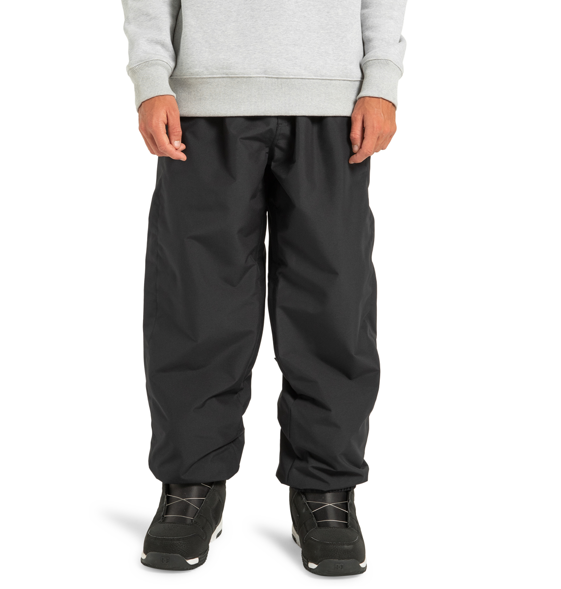 Model wearing DC Shoes Unisex Primo Snow Pants in black and a light gray sweatshirt, paired with black athletic shoes. Cropped below the shoulders, against a plain white background.