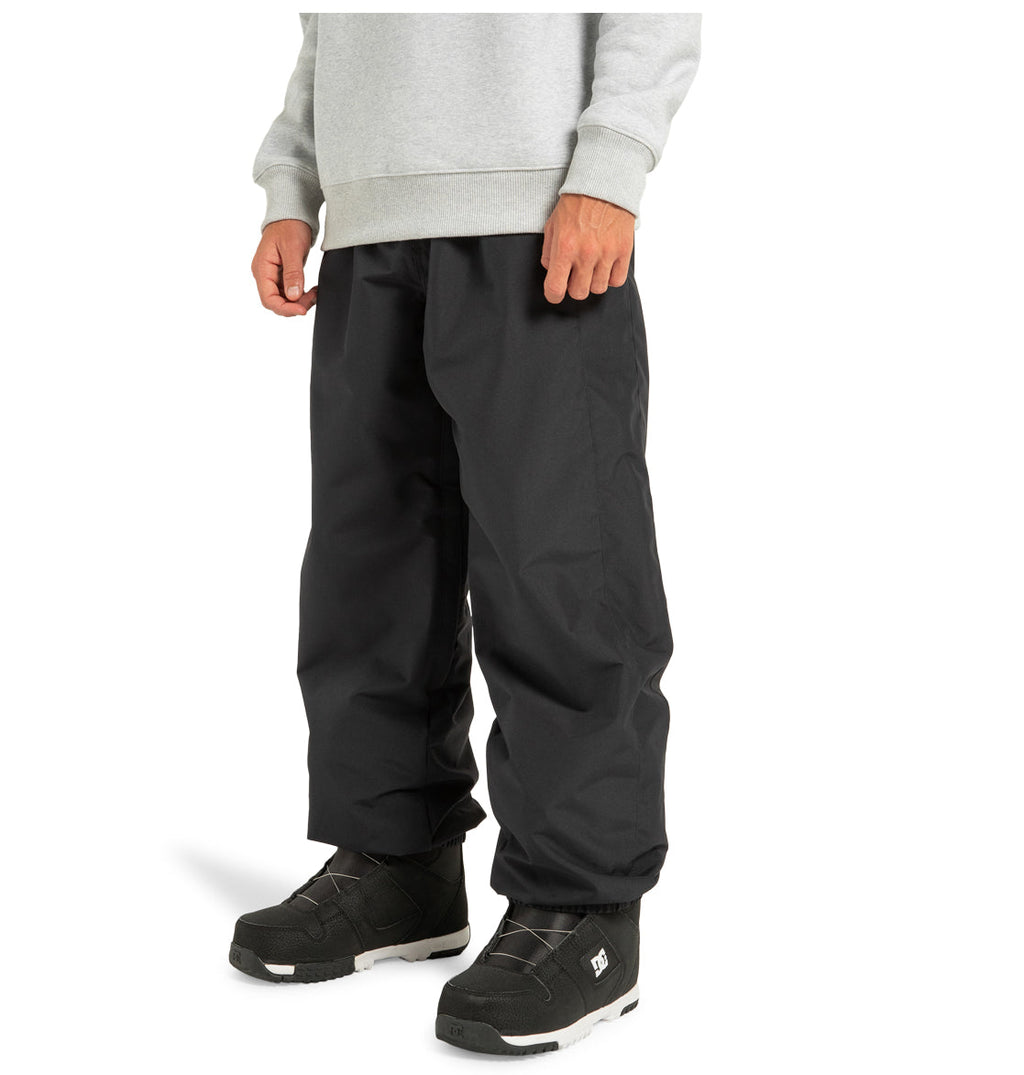 A person wearing a light gray sweatshirt, DC Shoes Unisex Primo Snow Pants in black made from recycled polyester, and black snow boots with white soles, standing against a plain white background.